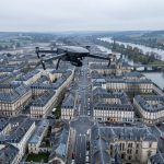 Quels recours choisir pour protéger ses libertés face aux drones policiers à Besançon ? Vue aérienne sobre de Besançon avec un drone de surveillance au-dessus d’une zone urbaine, dans une ambiance documentaire et institutionnelle.