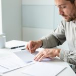 Comment déclarer un arrêt maladie et respecter les délais d’envoi ? Un salarié à domicile prépare des documents administratifs vierges et une enveloppe sur un bureau lumineux.